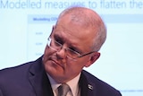 Scott Morrison tilts his head to the side during a press conference. A slideshow is visible on a screen behind him