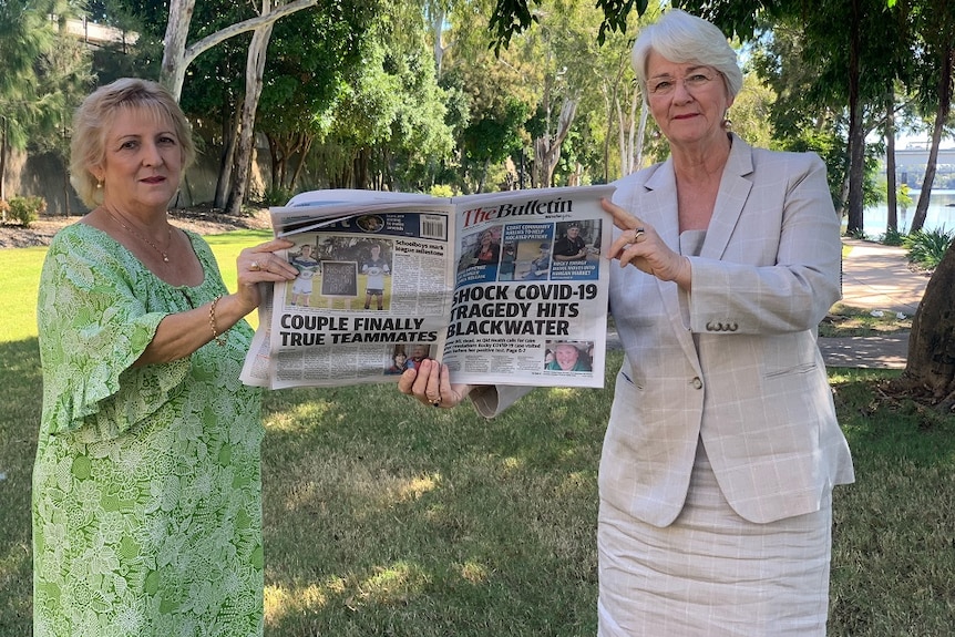 Michelle Landry in a green dress and Margaret Strelow and a neutral blazer and dress holding a copy of the Morning Bulletin.