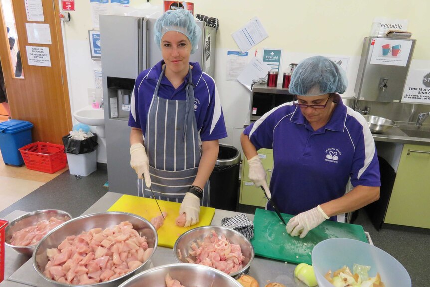 Two volunteers preparing chicken in the kitchen at the Waterbridge Food Co-Op