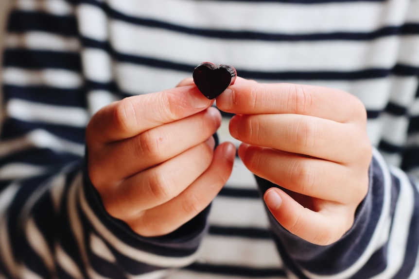 A pair of hands holds up a tiny thumb-sized heart-shaped gummy.