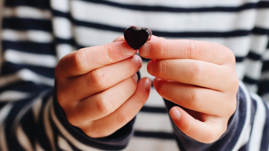 A pair of hands holds up a tiny thumb-sized heart-shaped gummy.