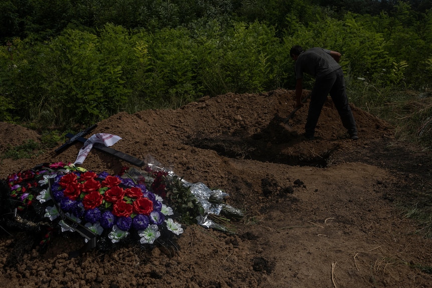 Мужчина намерен копать яму в земле лопатой.  На переднем плане цветы. 