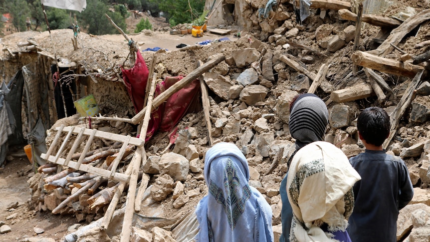 Afghan children stand near a house that was destroyed in an earthquake