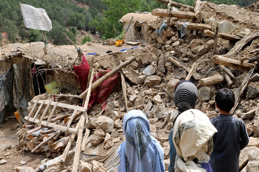 Children from Afghanistan stand near a house destroyed by an earthquake