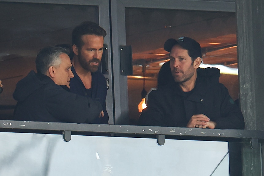 Wrexham co-owner Ryan Reynolds speaks to Joe Russo and Paul Rudd in the stands at a Wrexham game.