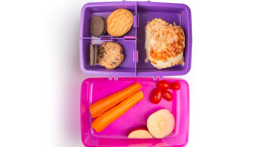 A ham pizza scroll, a carrots, cherry tomatoes, chopped apple and biscuits in a purple lunch box.