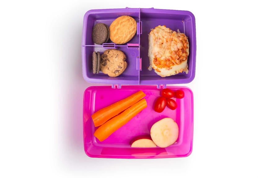 A ham pizza scroll, a carrots, cherry tomatoes, chopped apple and biscuits in a purple lunch box.