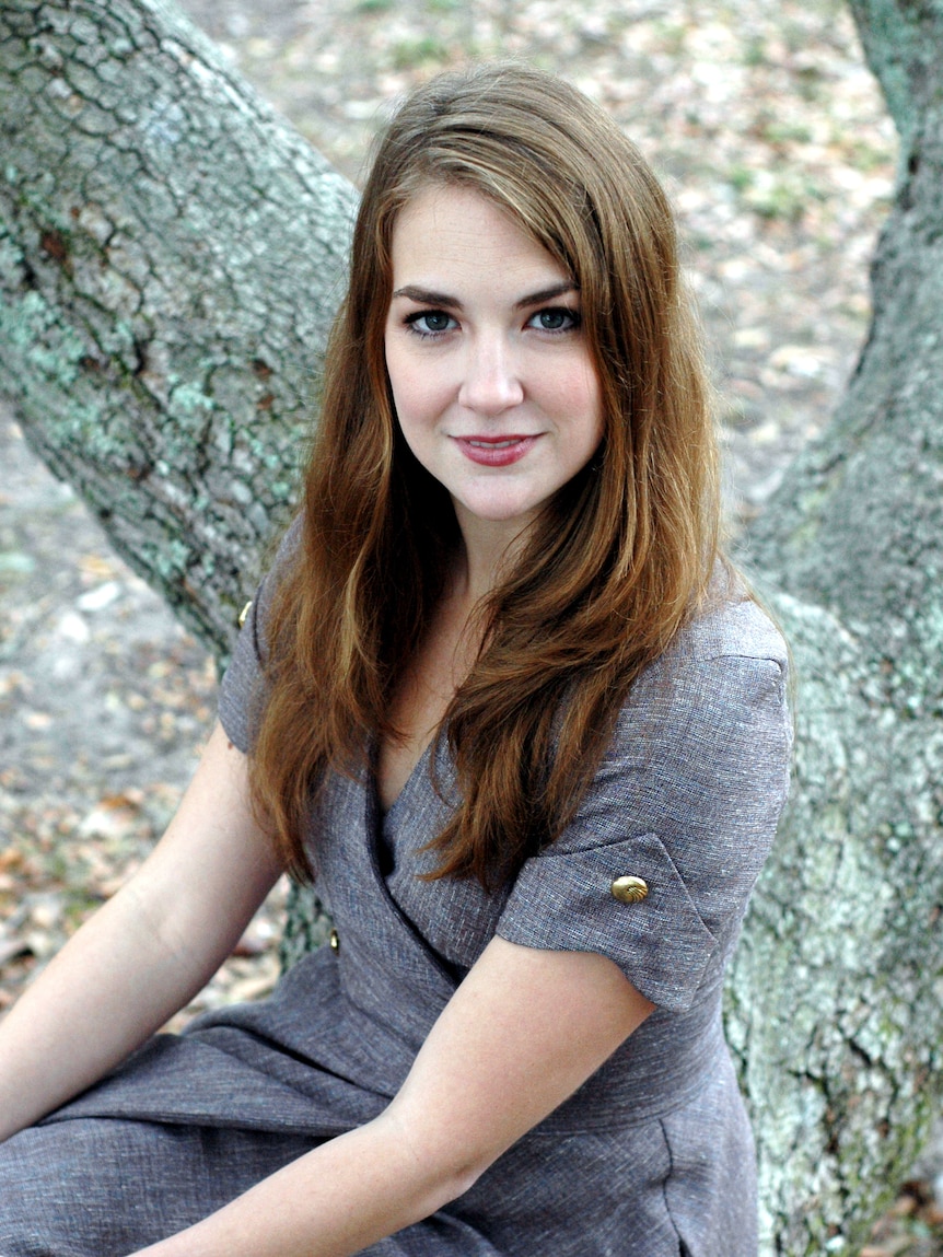 Portrait of a young woman outdoors with light long brown hair in a grey dress.
