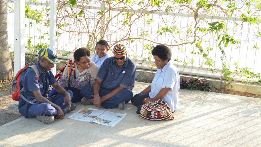 5 PNG locals sitting on the floor reading a newspaper together