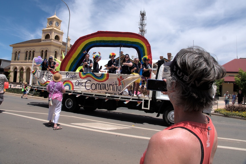 A truck filled with young kids and young adults drives past onlookers on a main street.