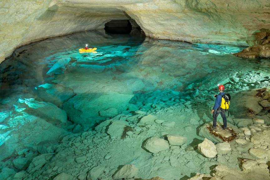 Turquoise water in a cave lake with two explorers - one is on a kayak. 