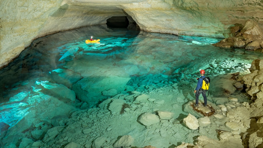 Turquoise water in a cave lake with two explorers - one is on a kayak. 