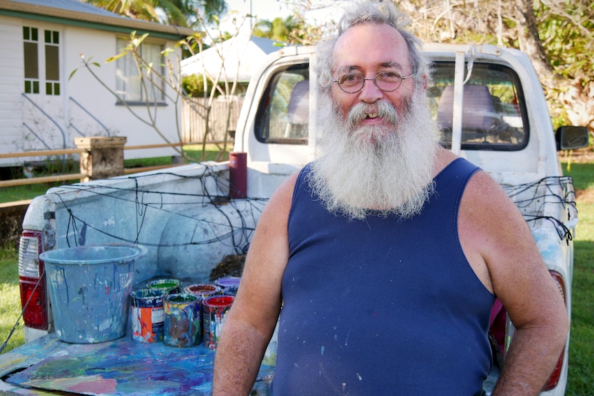 A bearded man sits on the end of a ute tray covered with paint