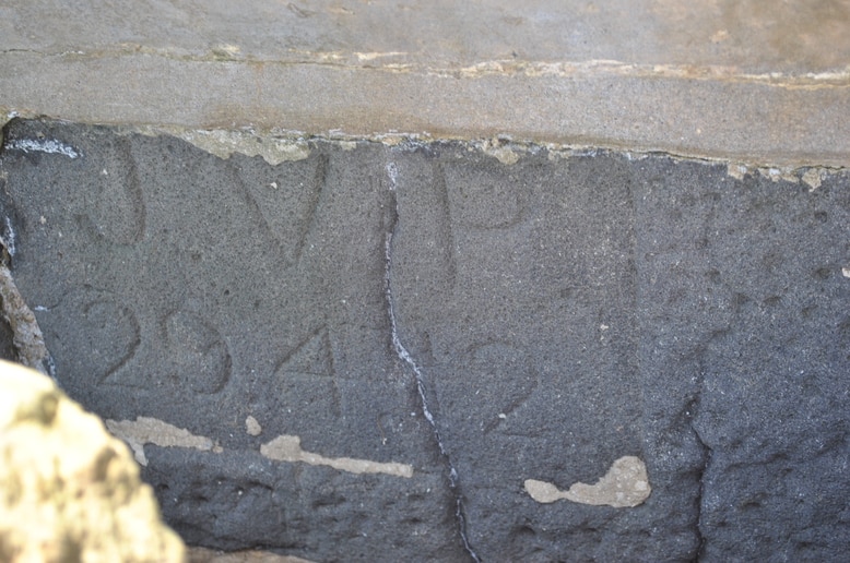 A close-up image of a bluestone cobblestone showing the highly-weathered engraved initials JVP.