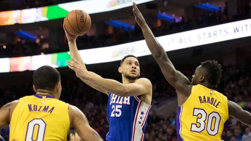 Philadelphia 76ers' Ben Simmons (25) shoots while being guarded by two LA Lakers players.