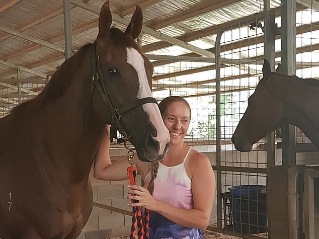 Melanie Tyndall pats a horse inside a stable.