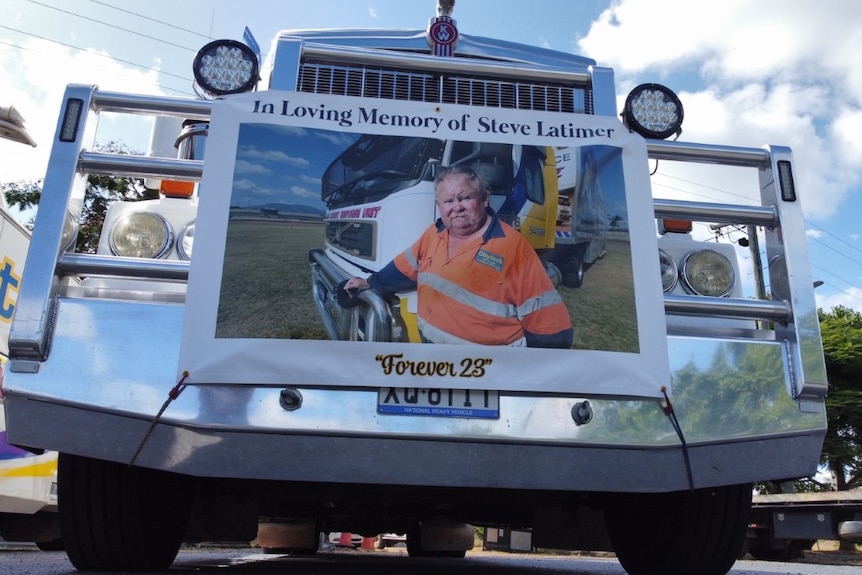 A truck with a photo of a man in high vis standing in front of another truck