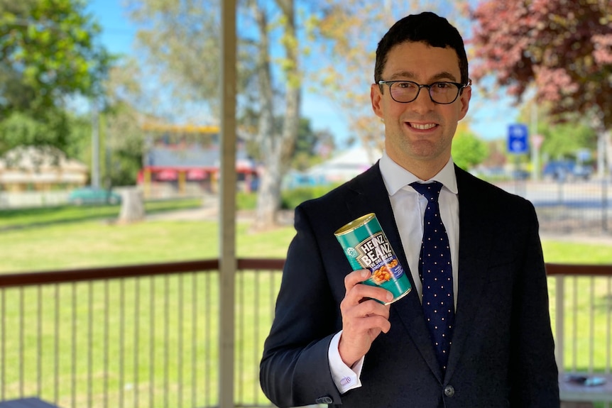 A man wearing a suit holding a can of baked beans