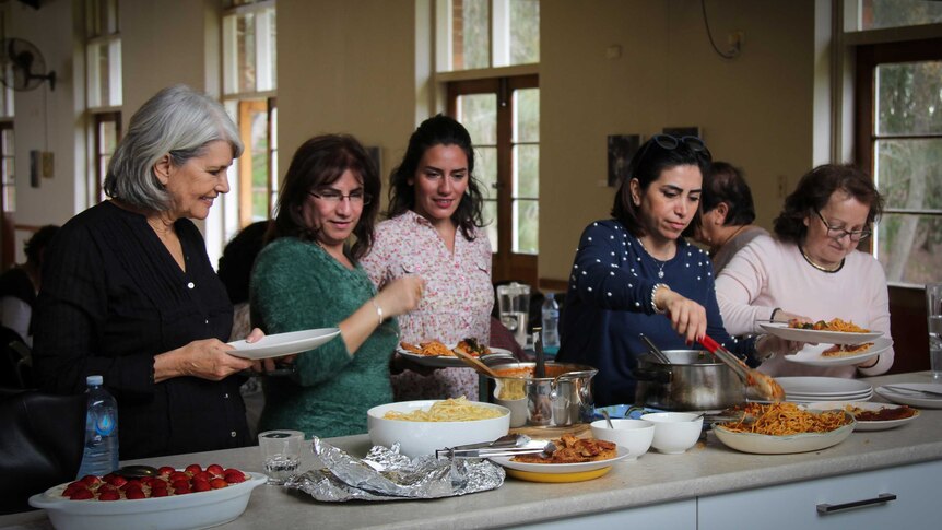 Five women serving themselves some food over a counter.