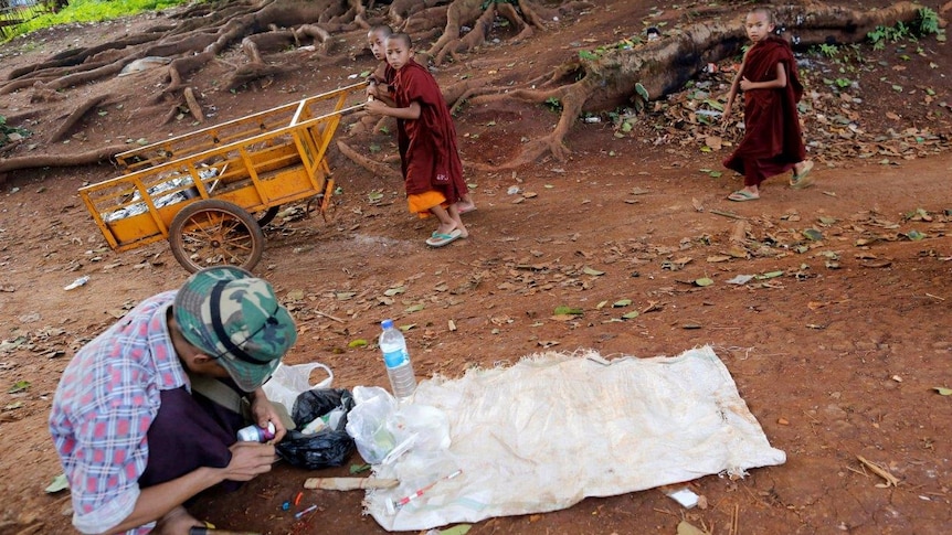 Buddhist novice monks walk past a drug user in Man Sam, northern Shan state, Myanmar
