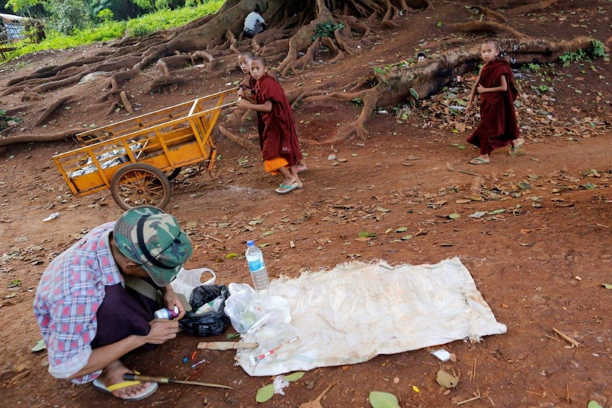 Buddhist novice monks walk past a drug user in Man Sam, northern Shan state, Myanmar