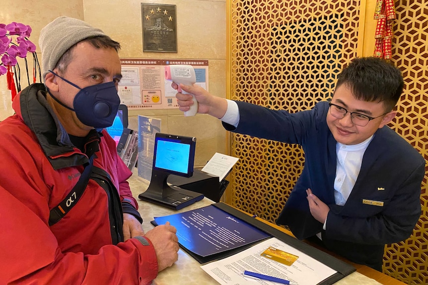 Man holding temperature gun sensor to head of cameraman wearing mask.