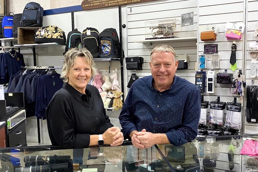 a women and a man stand behind a shop counter smiling 