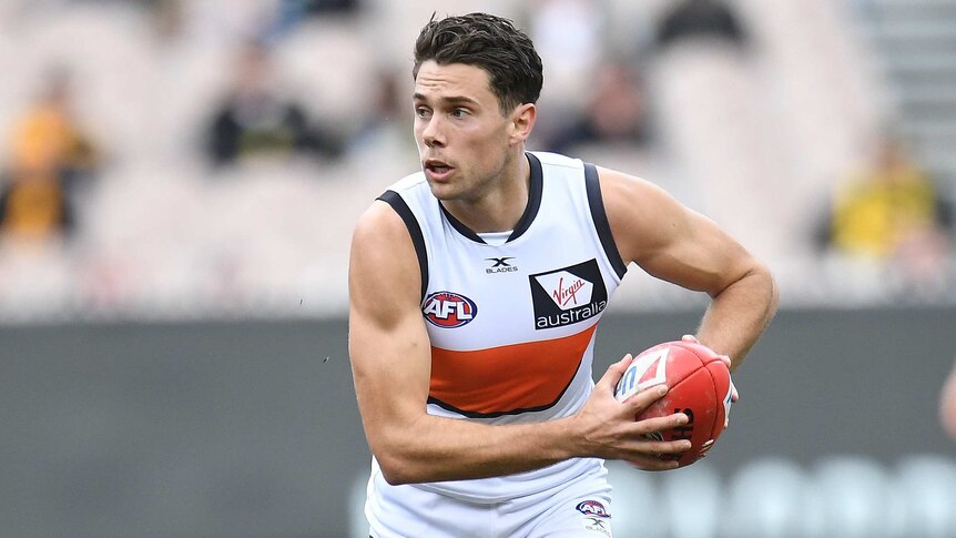 Josh Kelly holding a red AFL ball in both hands against Richmond.