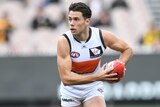 Josh Kelly holding a red AFL ball in both hands against Richmond.