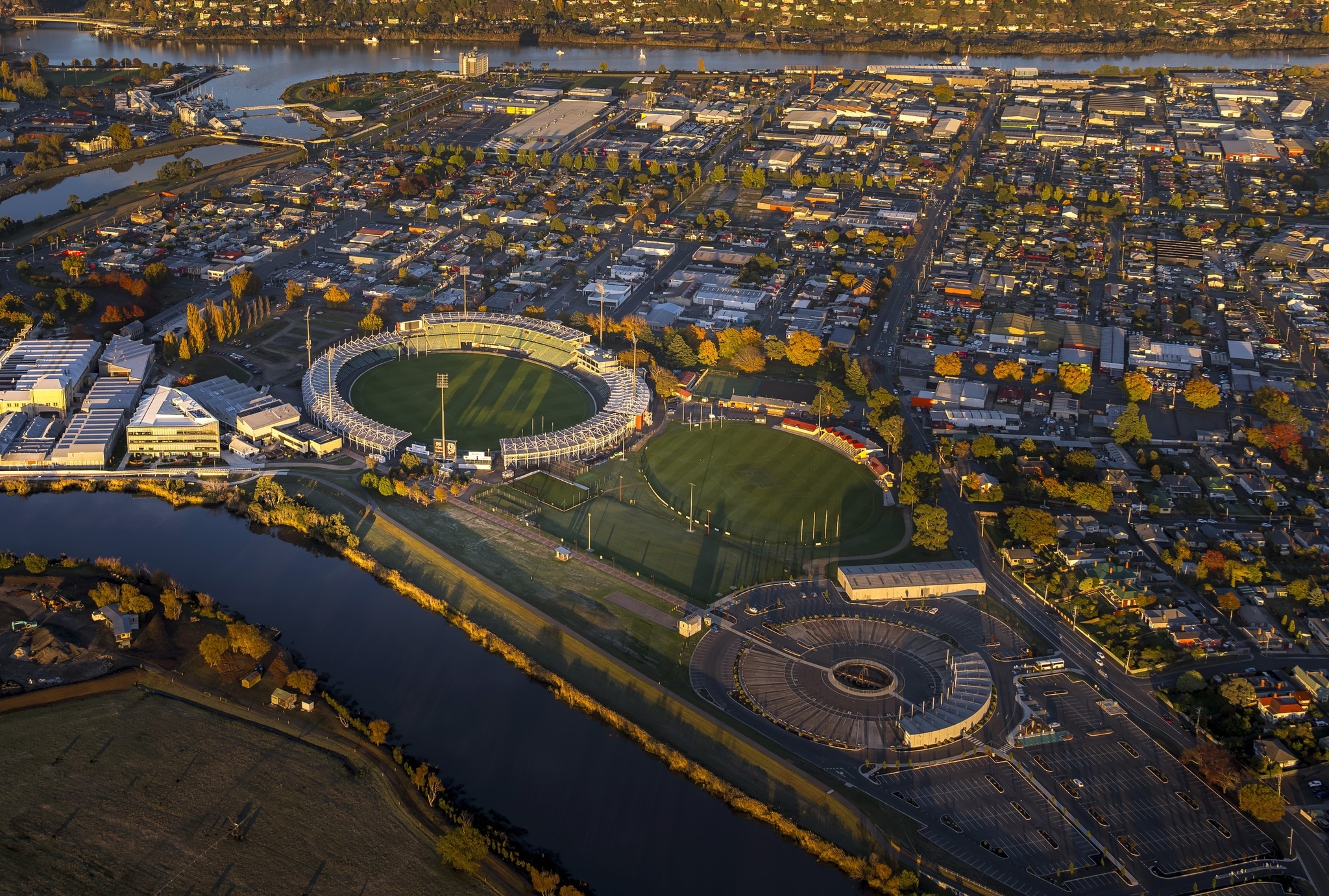 Imagem aérea de um oval esportivo e arredores de uma cidade perto de um rio.