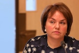 Senator Kimberley Kitching sitting in a Senate committee. She's wearing a navy blouse with white dandelions.