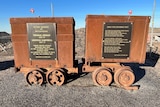 Two brown carts in grey sand with both carts covered in metal plaques with writing on them 