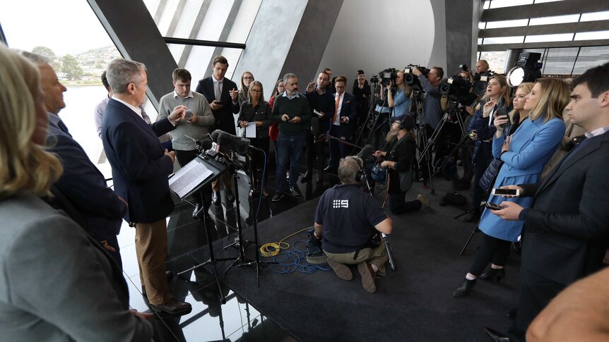 Mr Shorten stands at a podium responding to journalists standing in a half circle around him