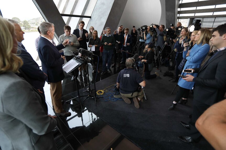Mr Shorten stands at a podium responding to journalists standing in a half circle around him