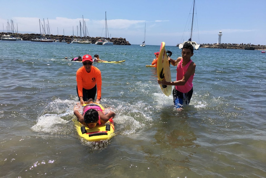 Two children swim to shore on foam surfboards.