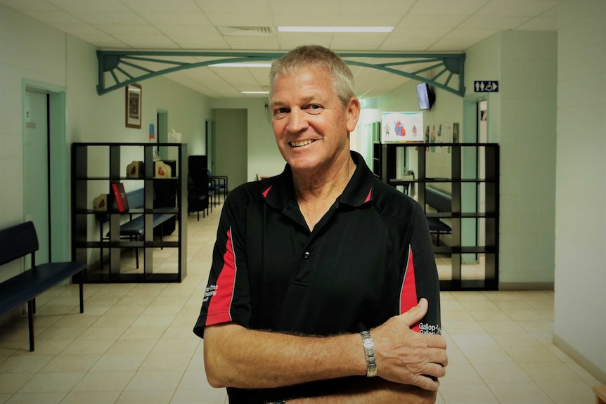 Man arms crossed smiling at camera in a waiting room. White walls.