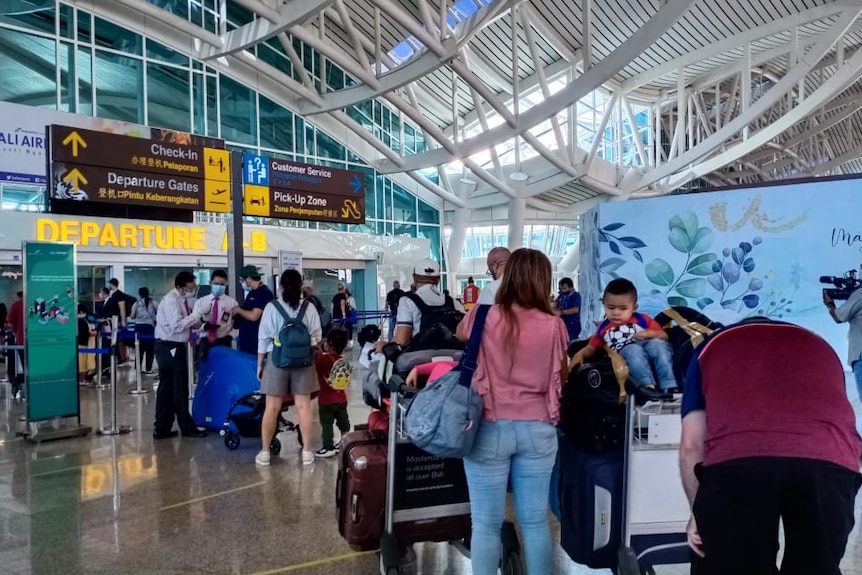 People line up with luggage at the departure gate at the Denpasar airport in Bali