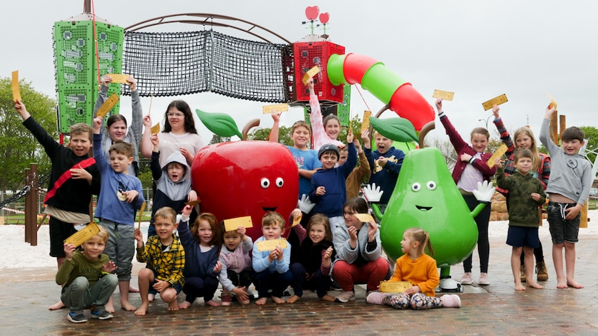 A group of children smiling and holding a yellow ticket in the air at a playground near a large plastic 