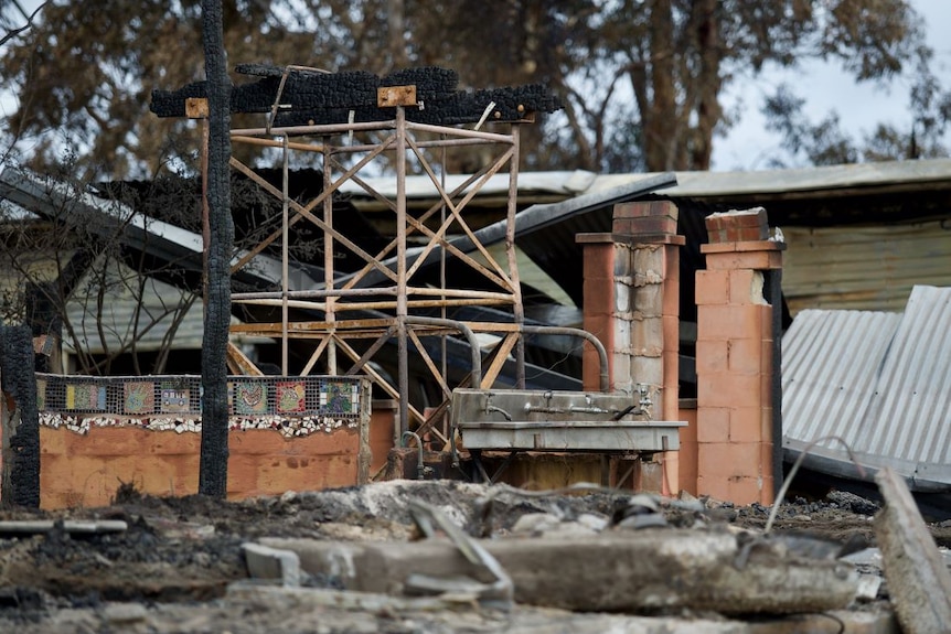 A burnt out building. All that's left is a row of drinking fountains above a metal trough and some mosaic tiles.