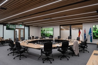 An empty round desk in an empty room with the Aboriginal, Australian and Torres Strait Islander flags in a corner by a window.