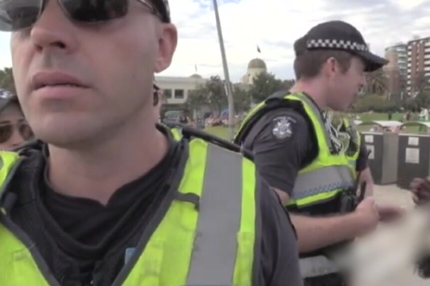 Police in high-visibility vests speak to people from both of the groups at the St Kilda foreshore.
