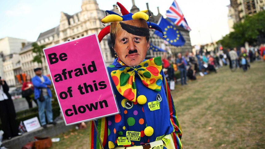 An anti-Brexit protester wearing a clown costume and a defaced mask depicting British Prime Minister Boris Johnson.