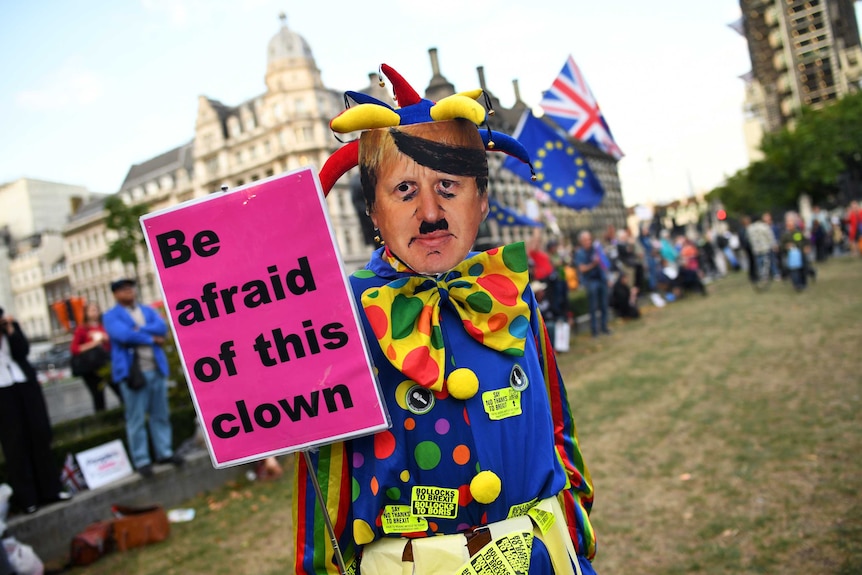 An anti-Brexit protester wearing a clown costume and a defaced mask depicting British Prime Minister Boris Johnson.