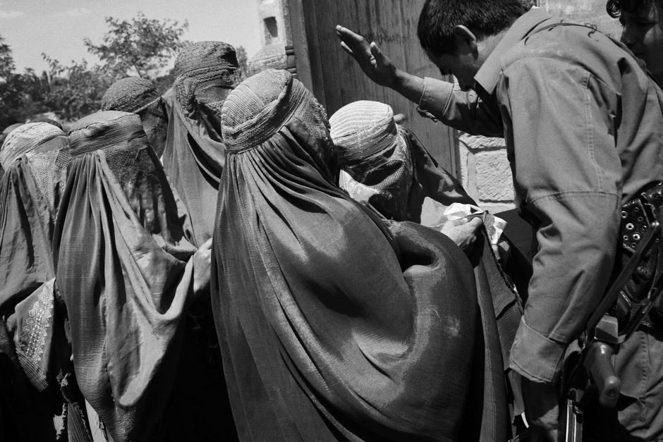 A policeman tries to contain women entering a mosque in Kunduz City where aid organisations are distributing packages.