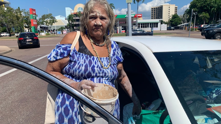 June Mills Gudbiling holding a white bucket looks at the camera as she stands near her car on a street in Darwin