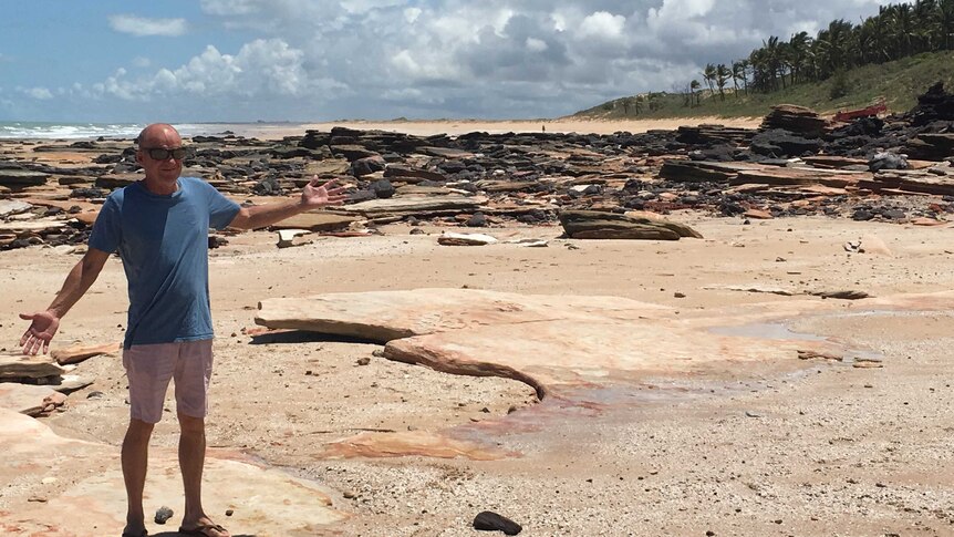 A man standing on a beach with exposed rocks in the background.