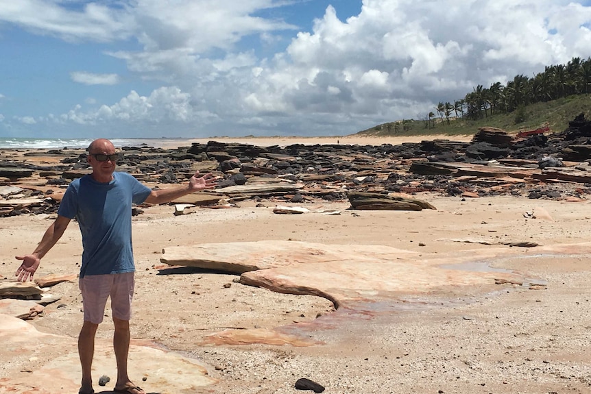 A man standing on a beach with exposed rocks in the background.