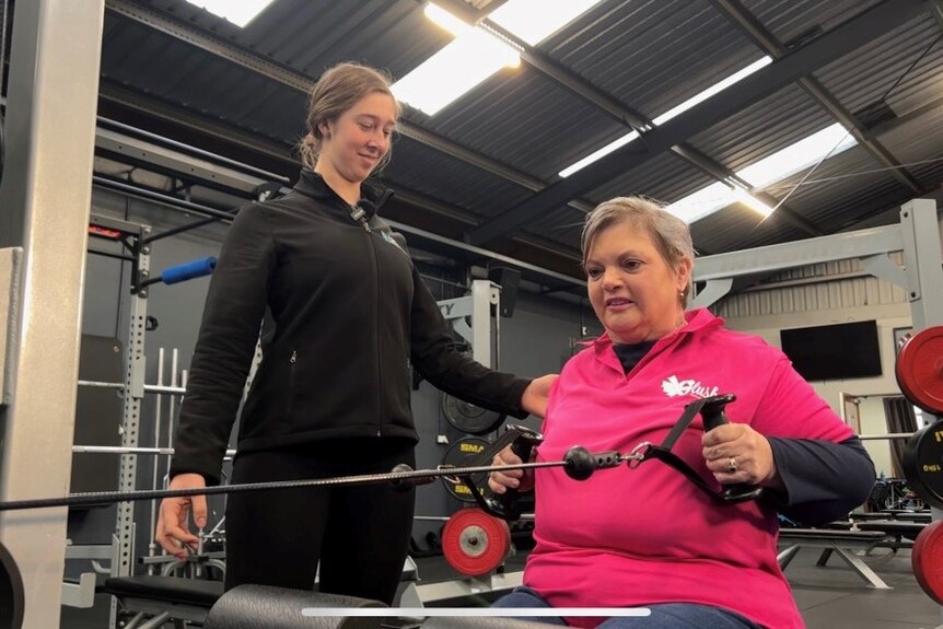 A woman exercising sitting next to a trainer