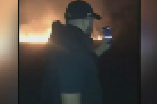 A man with a mobile phone as a fire burns in the background