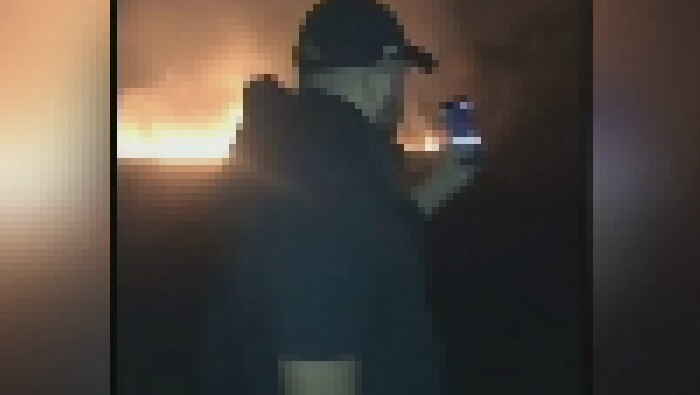 A man with a mobile phone as a fire burns in the background